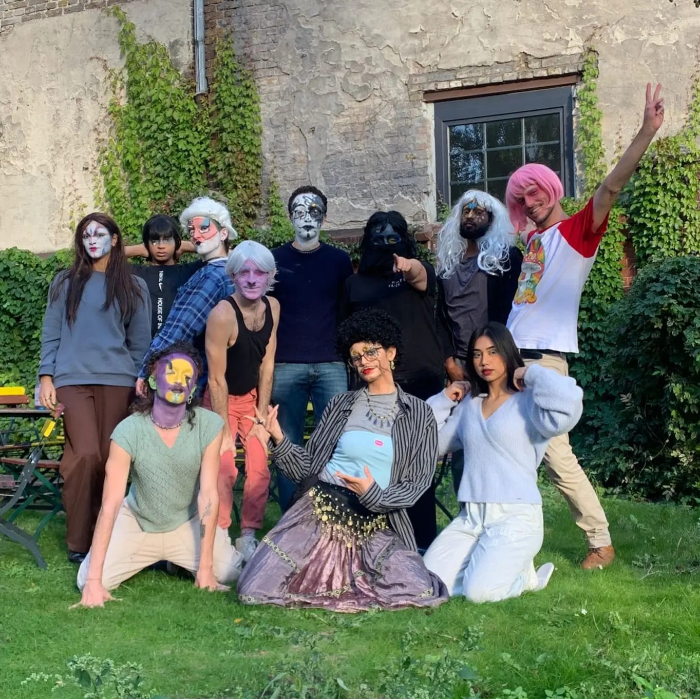 Eine Gruppe Teilnehmender der Queer*Yourope Berlinfahrt 2022 posen in Drag geschminkt und gekleidet als ihre bunten Drag-Personas vor einer Hauswand im Gras
